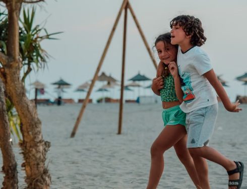 Two children enjoy a playful walk on a sandy beach, capturing summer fun.