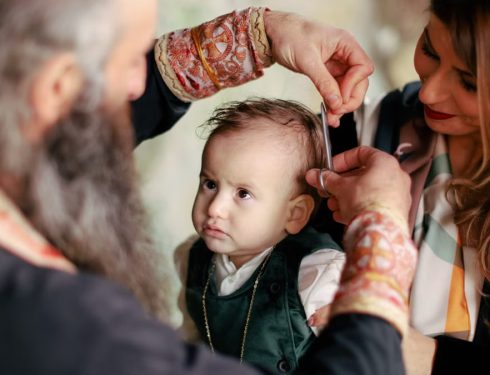A baby's first haircut performed during a religious ritual with parents and clergy present.
